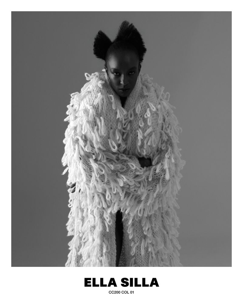 Black woman wearing a textured white fluffy knit coat against a plain neutral studio background