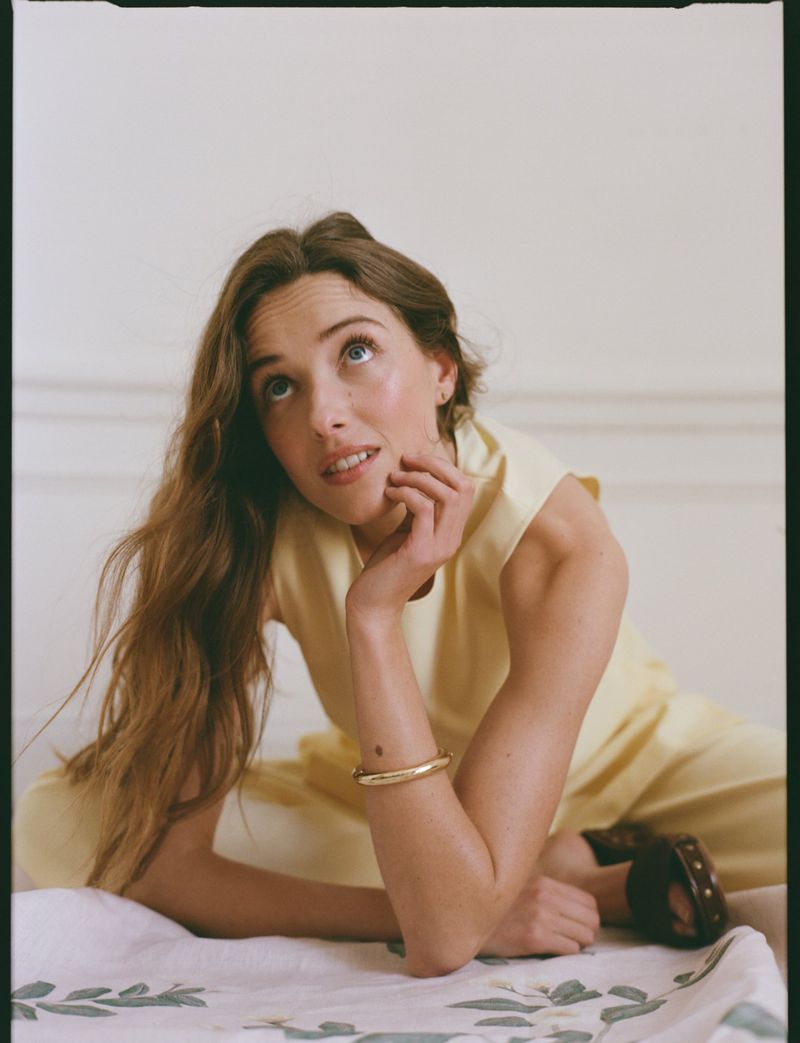 Woman in yellow sleeveless top and matching trousers sitting against a neutral wall for Tuckernuck Spring 2026