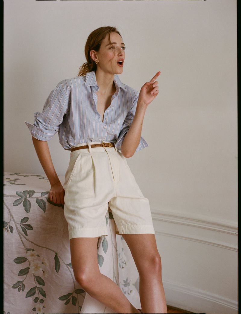Woman in blue striped button-down shirt and cream shorts leaning on a table for Tuckernuck Spring 2026