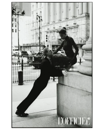Black and white fashion shot of a man and woman posing against city architecture in structured clothing in an outdoor setting.