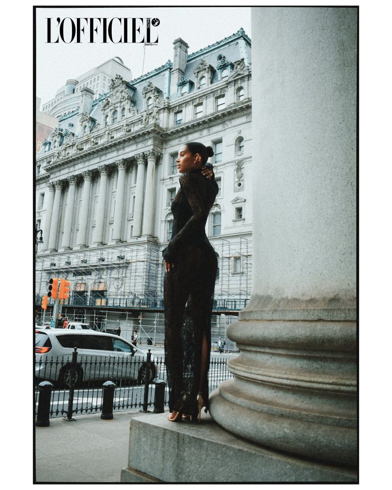 A model in an elegant black lace dress poses beside a grand building and a large white pillar in an urban fashion editorial shot.