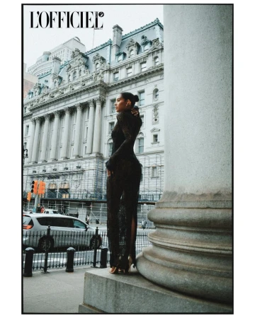 A model in an elegant black lace dress poses beside a grand building and a large white pillar in an urban fashion editorial shot.