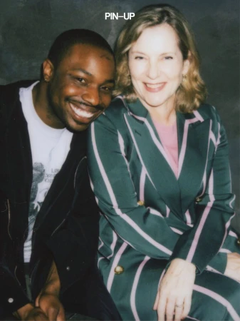 A smiling Black man leaning on a smiling white woman wearing a dark green striped suit for PIN-UP Magazine