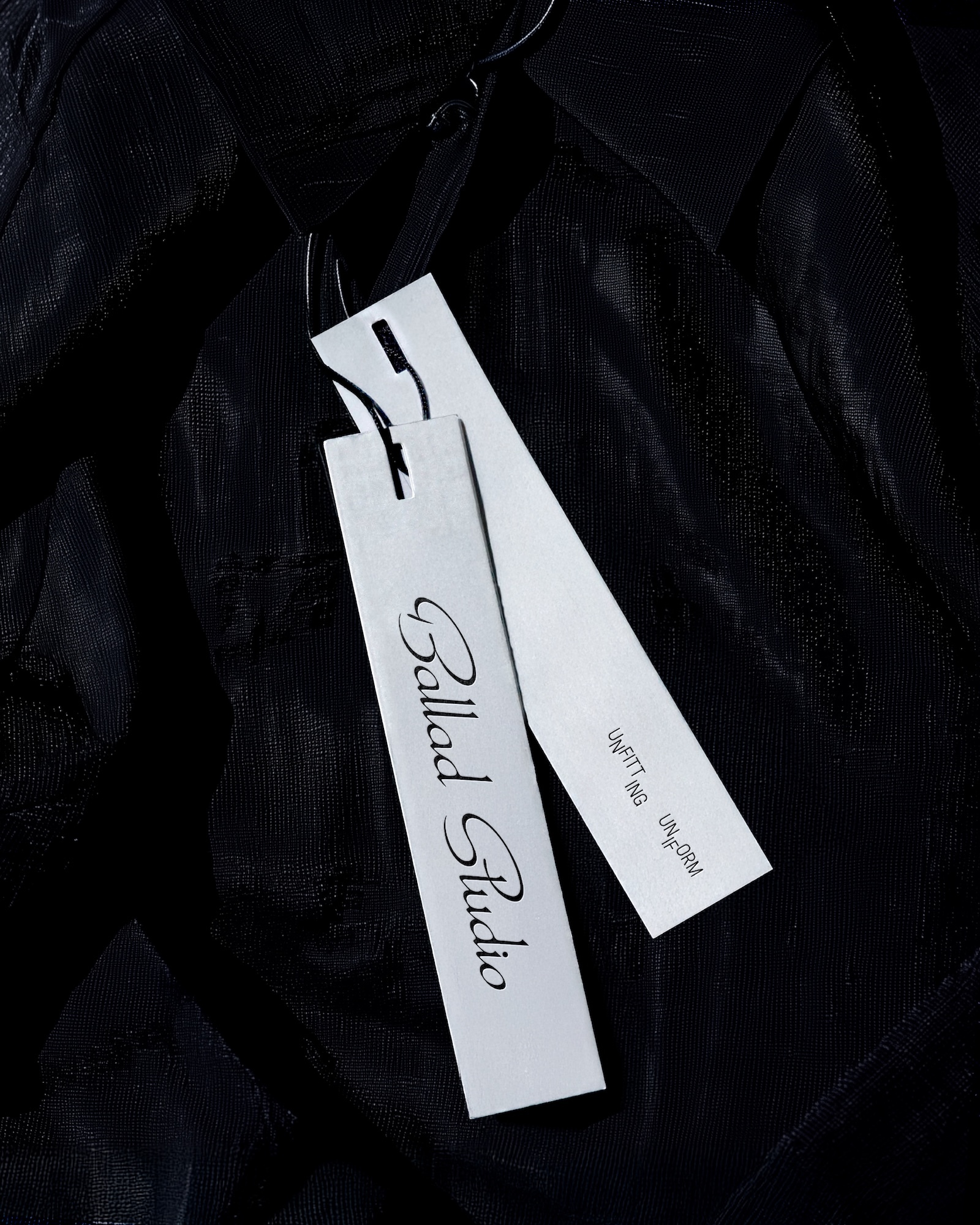 Two white paper clothing tags attached to a sheer black garment with visible brand text Ballad Studio