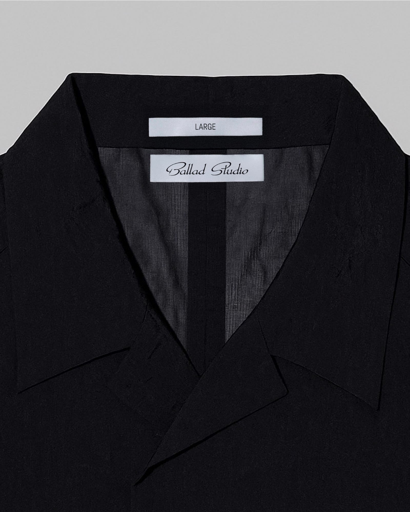 Close-up of a black collared shirt showing interior branded labels for Ballad Studio against a grey background