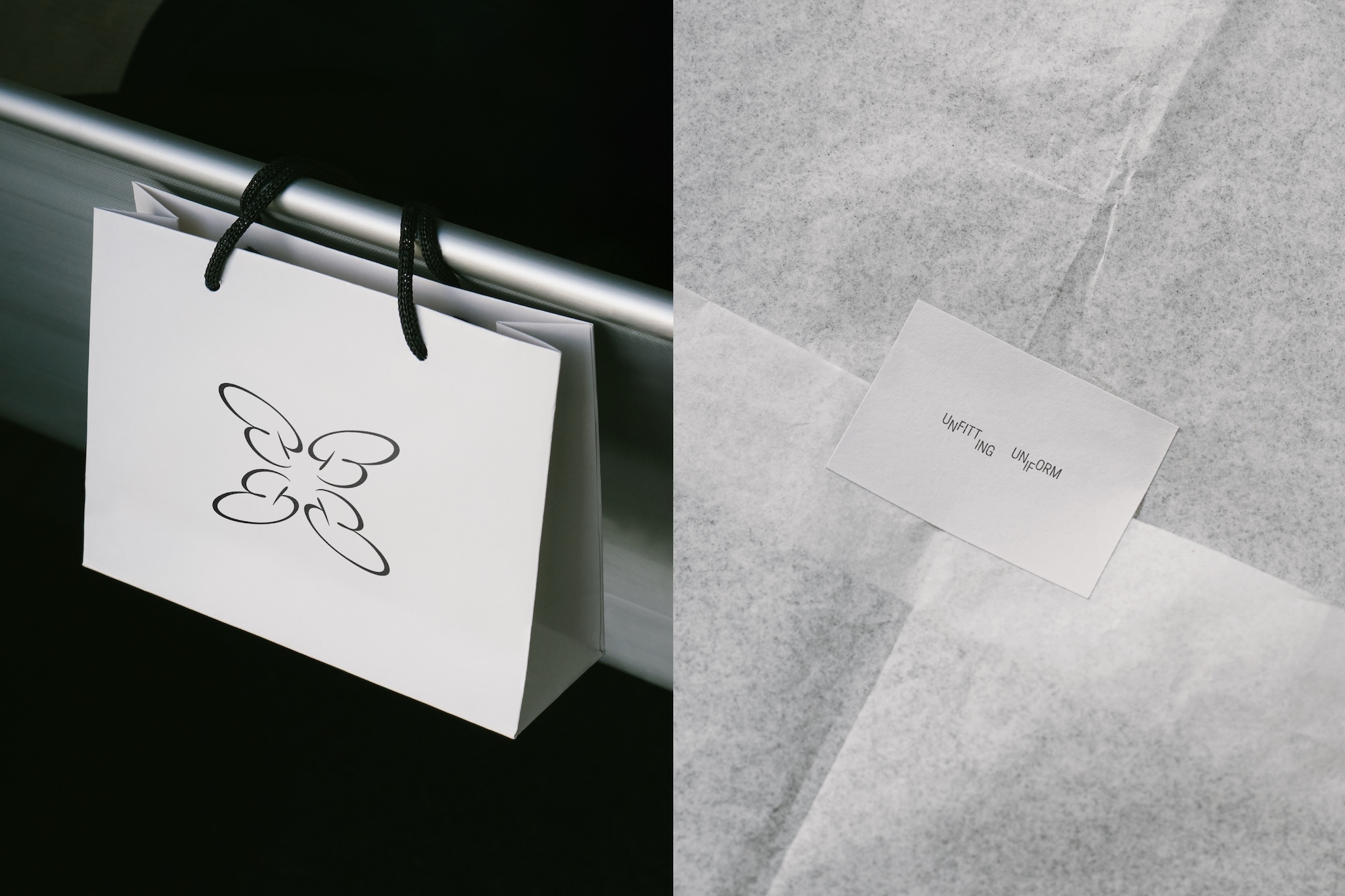 White paper shopping bag with black handles and a logo resting against a dark surface next to tissue paper with a small card.