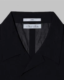 Close-up of a black collared shirt showing interior branded labels for Ballad Studio against a grey background