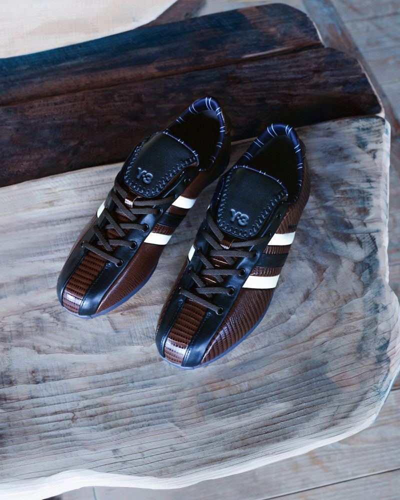 A pair of brown and black leather sneakers with white stripes placed on a rustic textured wooden surface.
