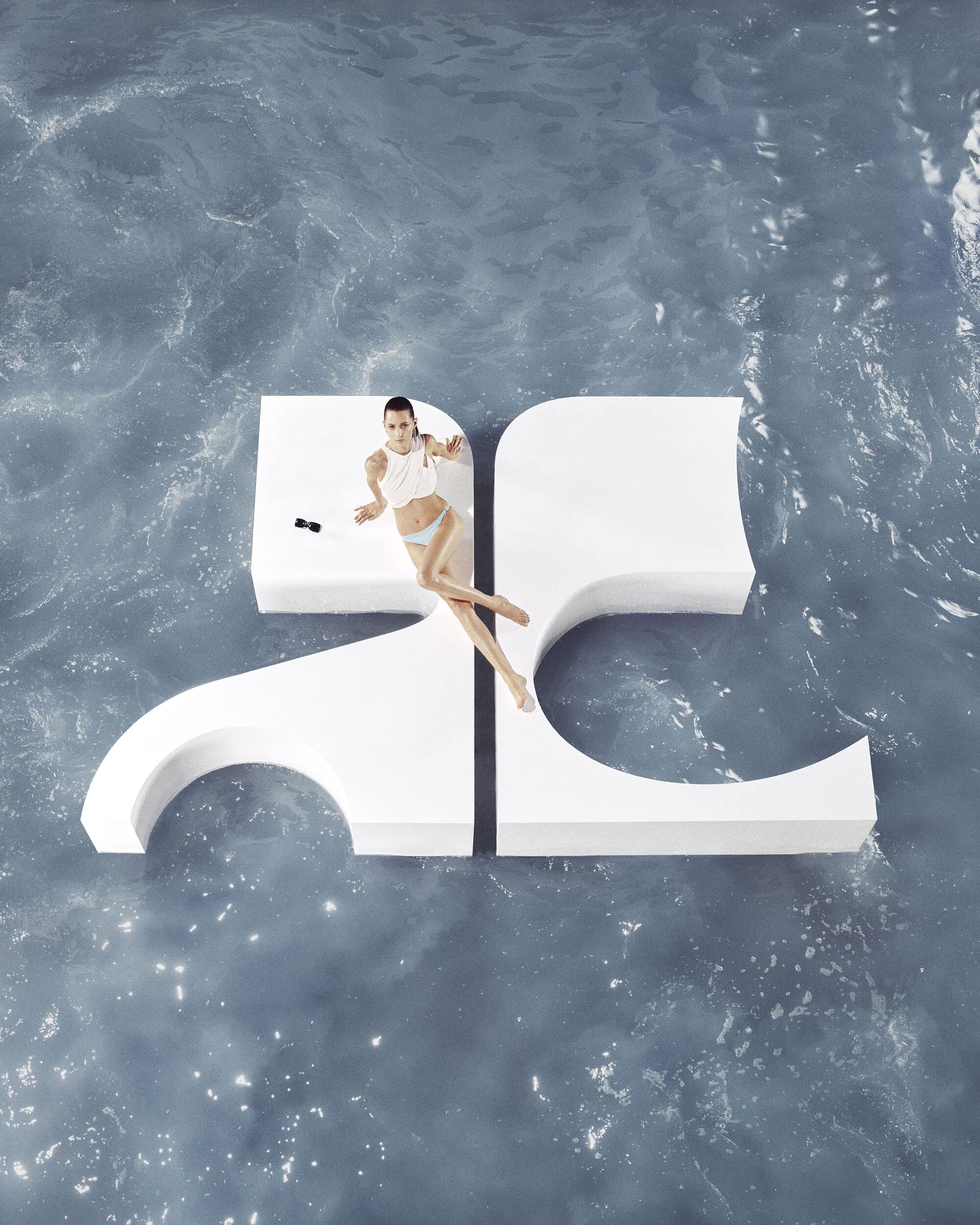 Woman in swimsuit poses on large geometric prop floating in water, captured from an overhead angle showcasing a unique fashion editorial.