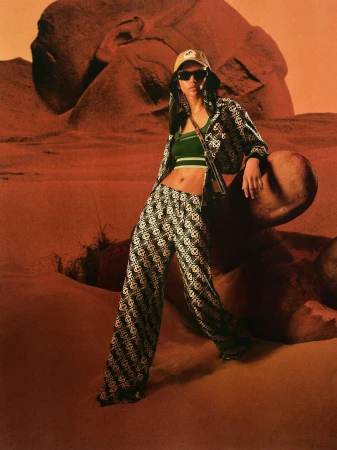 Model wearing a matching patterned tracksuit and cap posing outdoors against a desert landscape background.