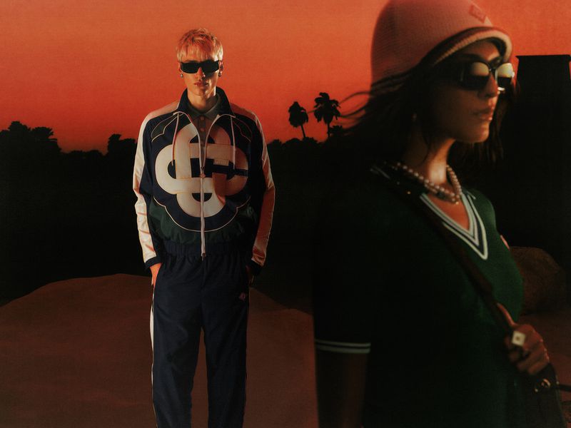 Two models posing outdoors at sunset for Casablanca Pre-Fall 26, wearing tracksuits and sunglasses against a desert landscape backdrop.