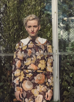 Portrait of Julia Garner wearing a floral print dress with a white collar outdoors near a greenhouse for Marie Claire Australia