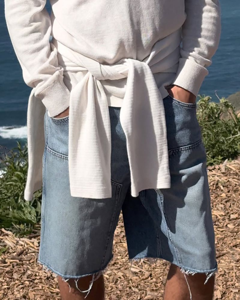 Close-up view of a person wearing light blue denim shorts and a white long-sleeve top tied around the waist outdoors.
