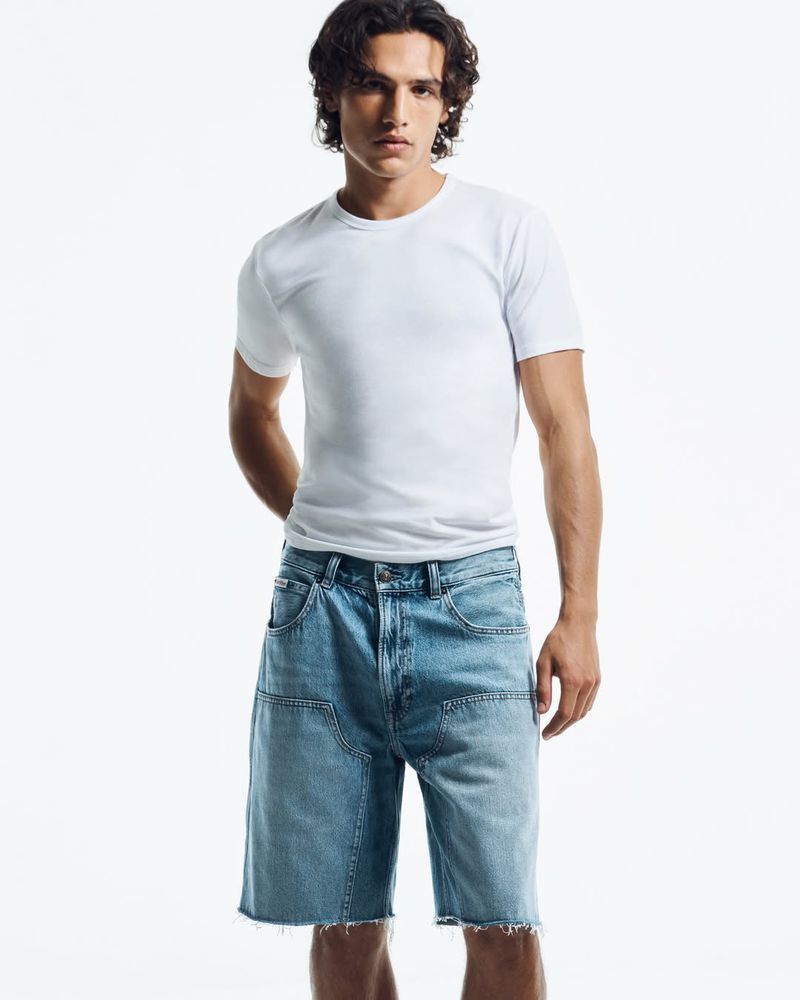 Model wearing a white t-shirt and denim shorts against a plain white background for Calvin Klein