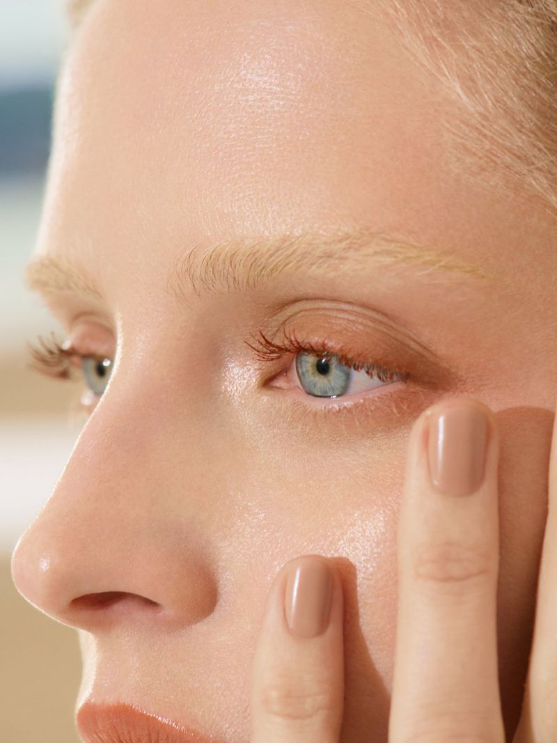 Close-up beauty portrait of a woman with blonde hair, light blue eyes, and nude nail polish, photographed by Theo Wenner for Chanel.