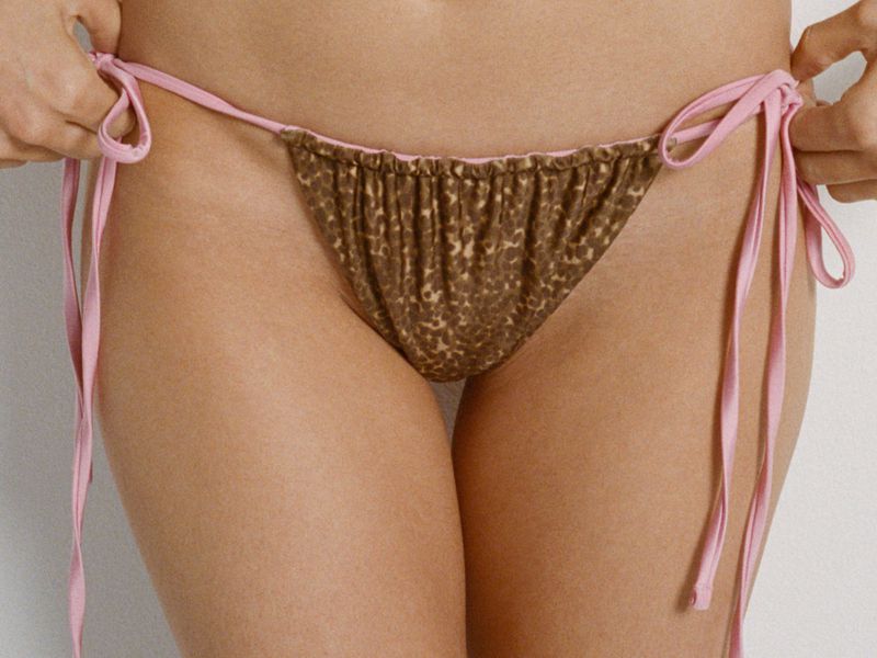 Close-up of a model wearing a pink-tied animal print bikini bottom against a plain white background