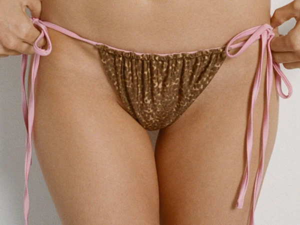 Close-up of a model wearing a pink-tied animal print bikini bottom against a plain white background