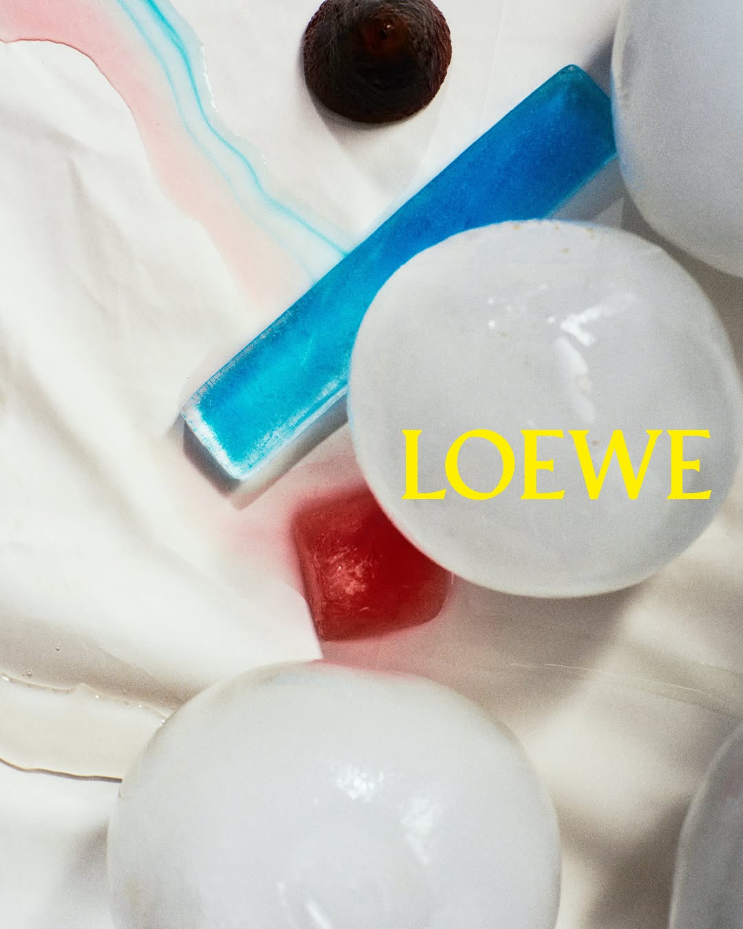 Yellow Loewe logo over frosted white spheres, a translucent blue bar, and colored liquid details.