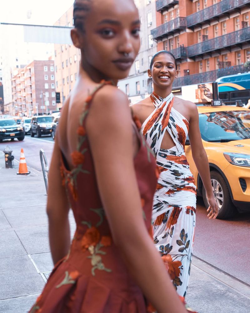 Two Black female models walking along a city street past a yellow taxi cab for the Saks Summer 2026 campaign.
