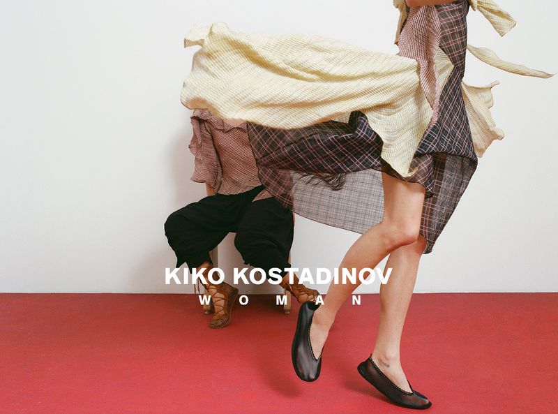 Model in motion wearing a patterned layered dress and black shoes against a white and red studio background