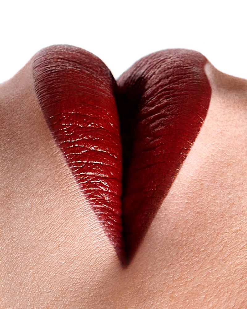 Extreme close-up of glossy dark red lipstick on lips against a bright white background