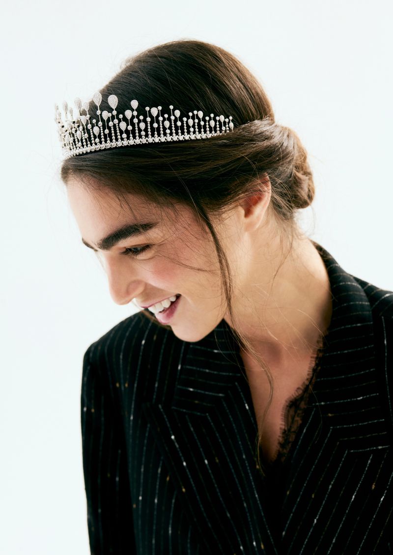 Model wearing a diamond tiara and black pinstripe jacket against a bright white background