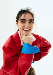 Smiling woman wearing a red jacket with blue cuffs and a metallic headpiece against a white background