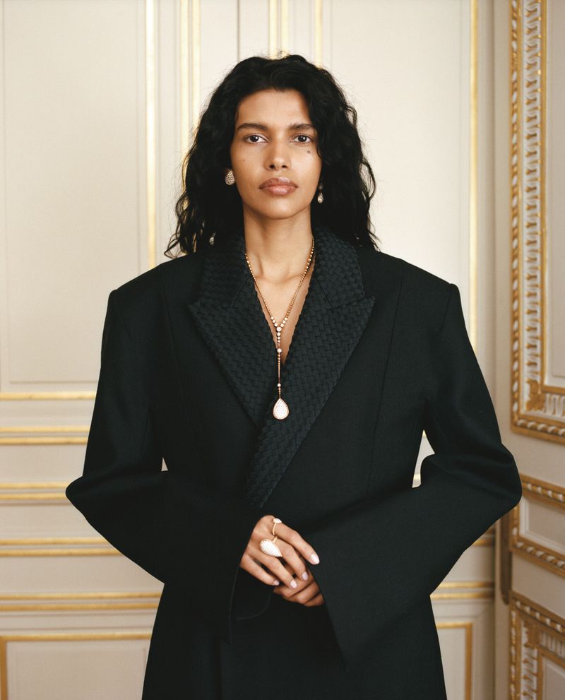 Model Pooja Mor wearing a black blazer and gold jewellery against a classic interior background