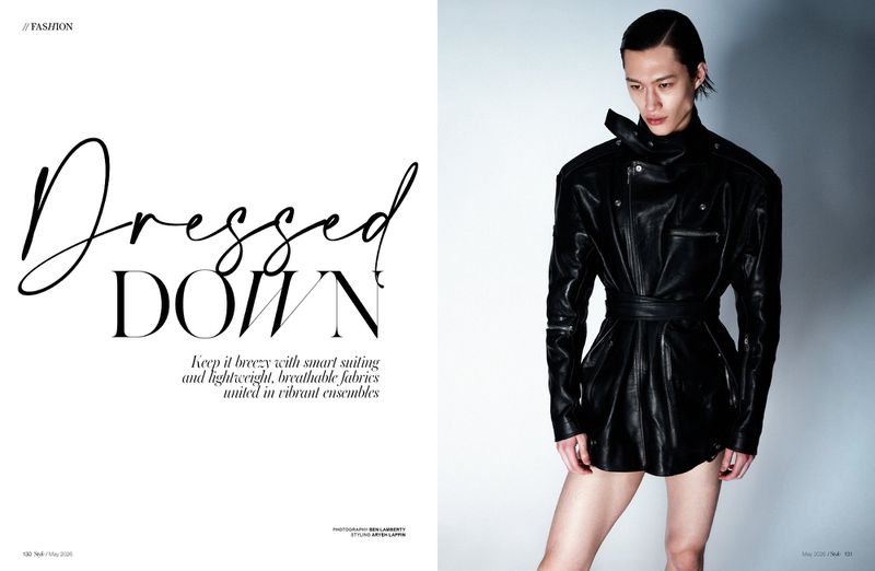 A male model wearing a black leather jacket and high-collar belt against a seamless light background for an editorial magazine spread.