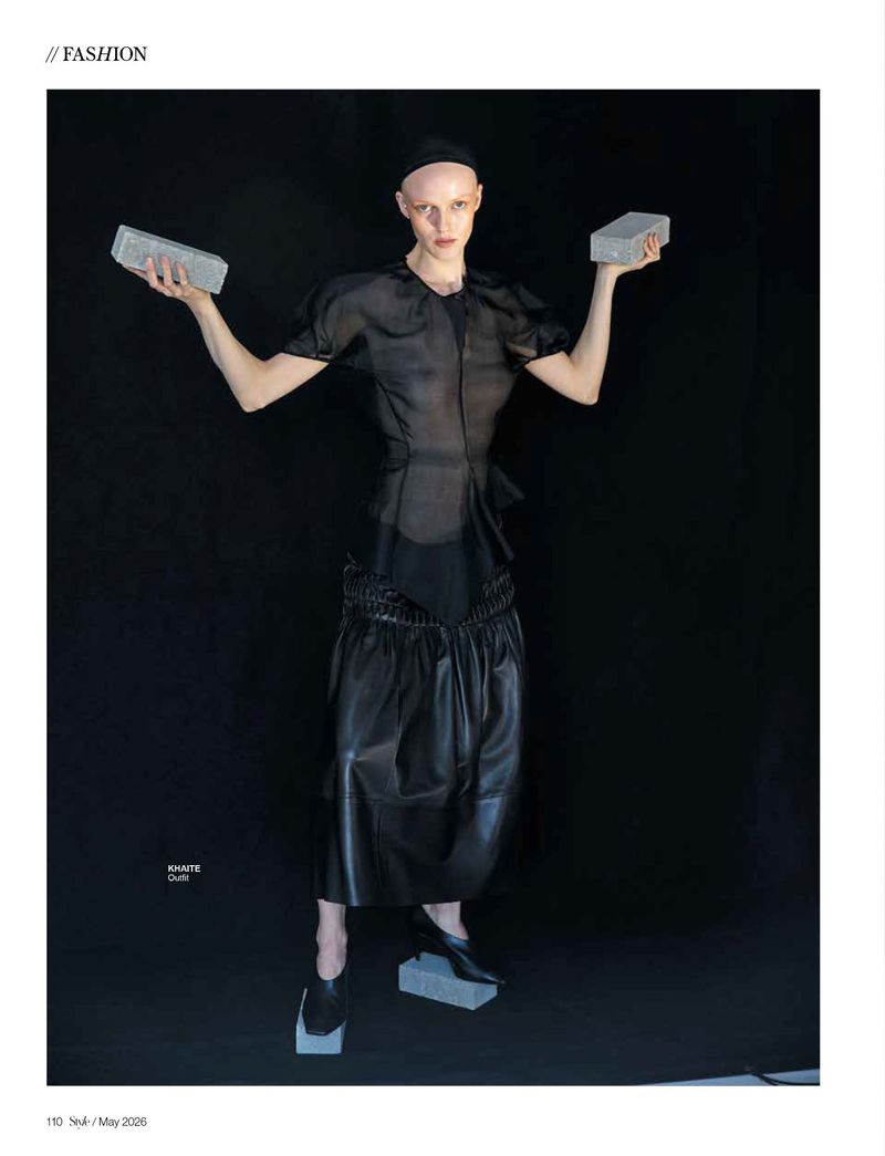 Model wearing a sheer black top and leather skirt holding two concrete bricks against a black background