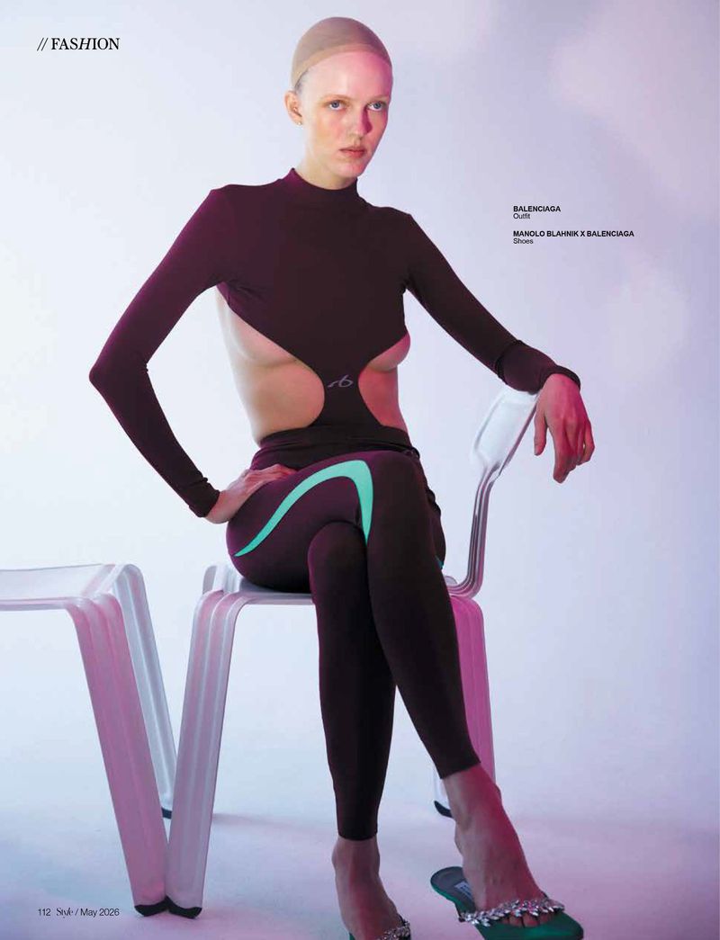 Model wearing dark cut-out long sleeve top and leggings seated on white chairs against a light studio backdrop