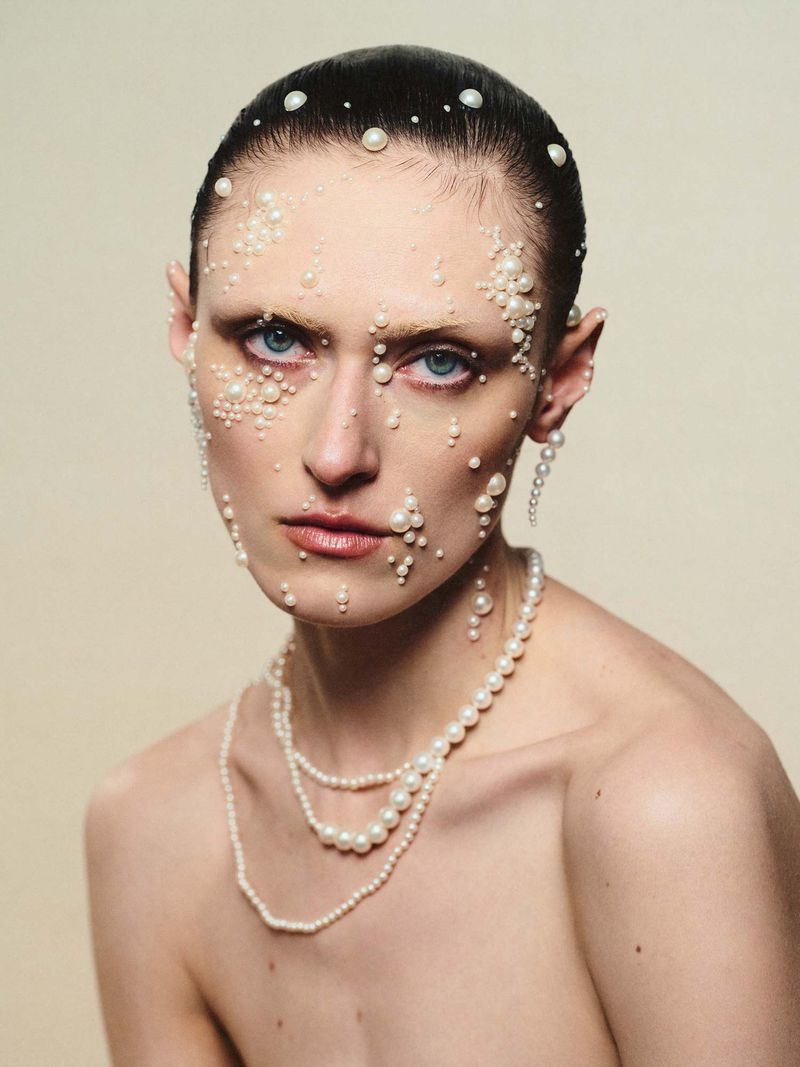 Close-up portrait of a model with pearls adhered to her face and hair, wearing layered pearl necklaces for Schön Magazine Nacre editorial