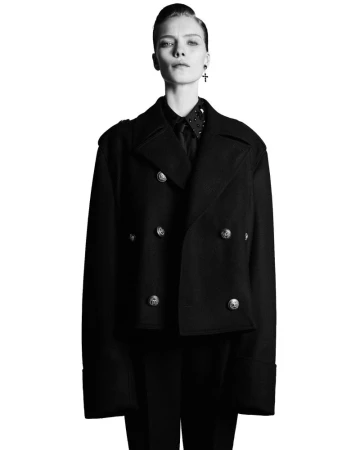 Model Penelope Ternes wearing a structured black double-breasted pea coat against a stark white background.