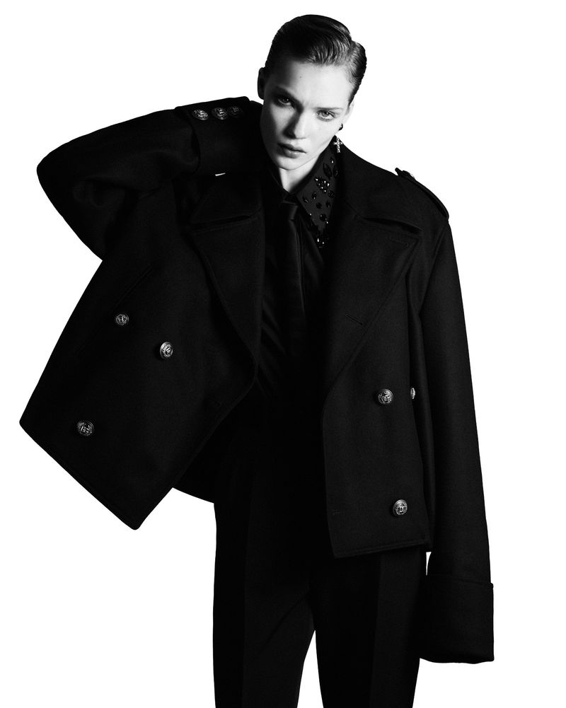 Model Penelope Ternes wearing a black double-breasted coat and trousers against a white background.