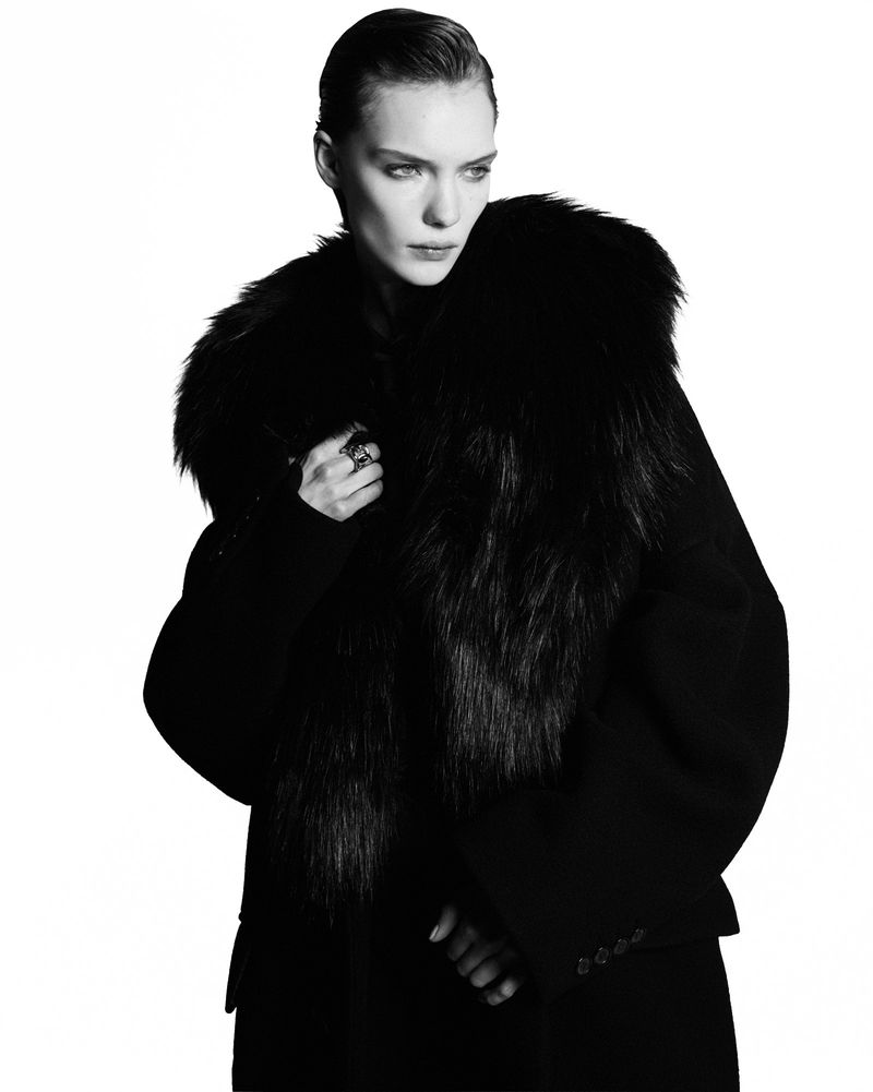 Model Penelope Ternes wearing a dark fur-collared coat against a pure white background in a studio fashion portrait.