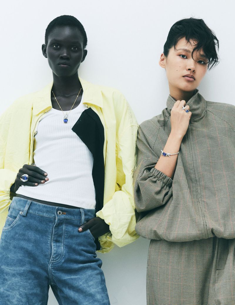 Two fashion models posing against a white studio background, wearing layered casual clothing and jewelry.