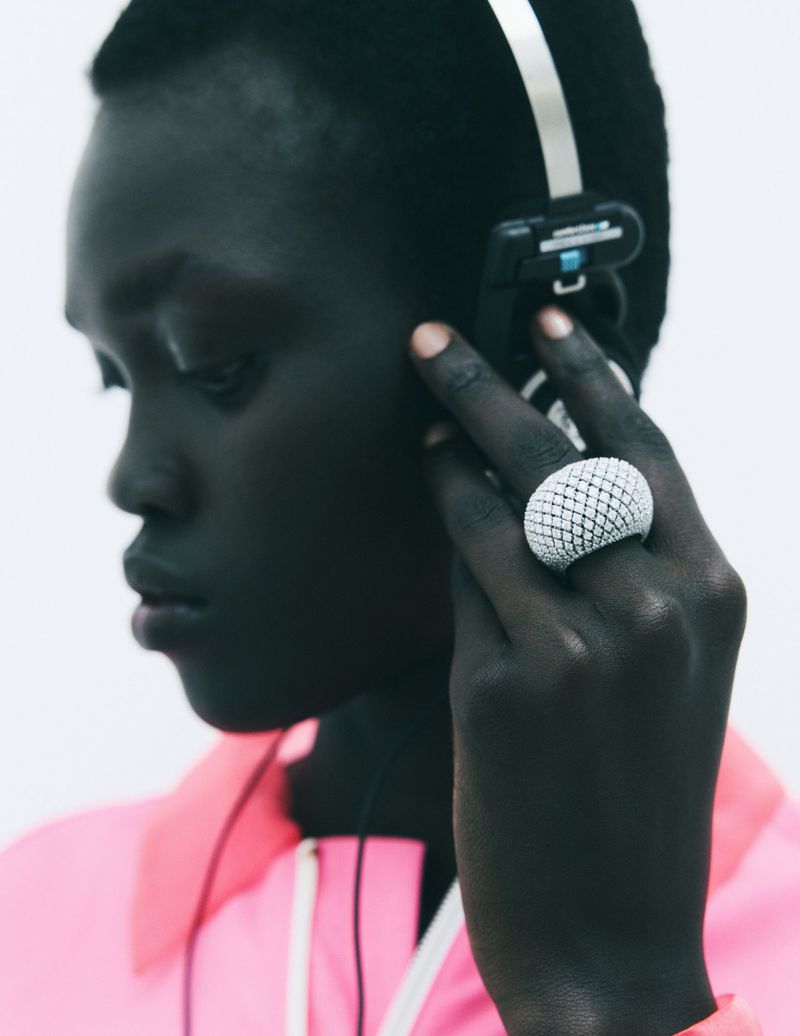 Close-up of a black woman wearing headphones and a large white statement ring against a white background