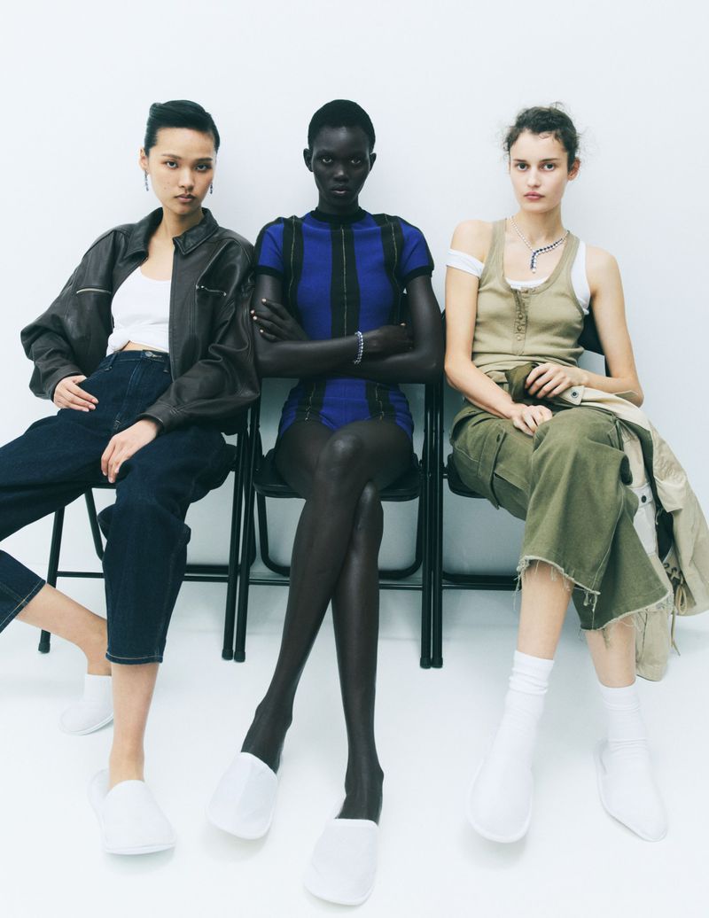 Three female models wearing casual fashion clothing and white slippers seated on black chairs against a white background