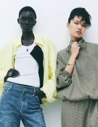 Two fashion models posing against a white studio background, wearing layered casual clothing and jewelry.