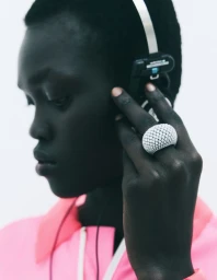 Close-up of a black woman wearing headphones and a large white statement ring against a white background