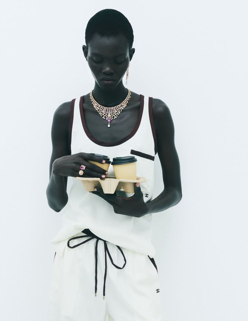 Model in white sleeveless top holding a cardboard coffee carrier tray against a white background