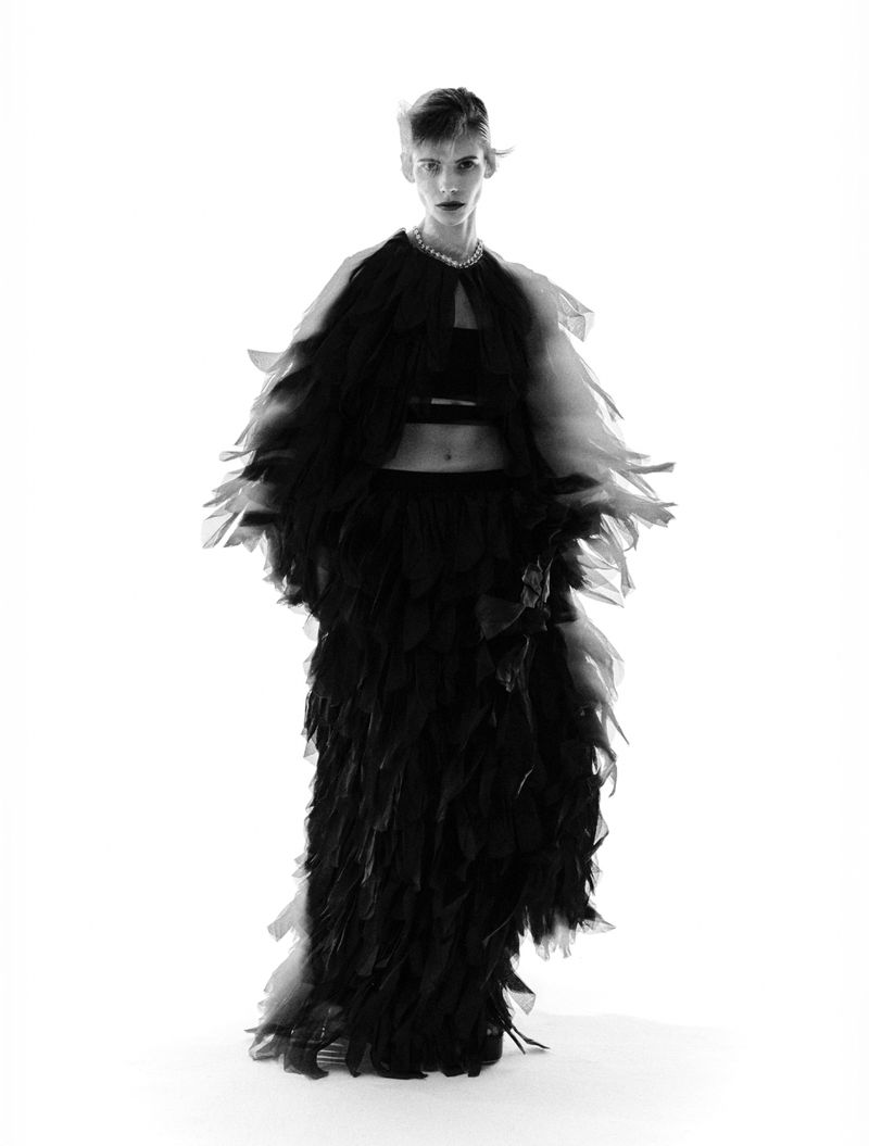 Model wearing a black feathered voluminous dress and necklace against a white background