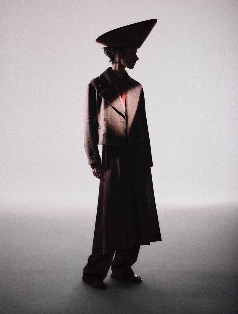 Model wearing a structured hat, cropped jacket, and long trousers against a seamless light background for L'Officiel Italia.
