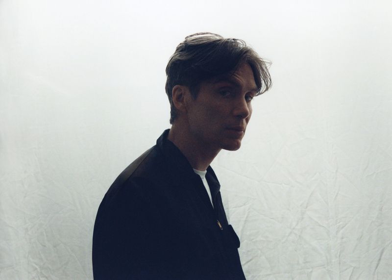 Portrait of adult male in a dark jacket over white shirt, glancing to the side against a diffused white backdrop.