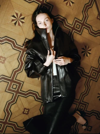Model lying on an intricate geometric patterned wooden floor wearing a black leather jacket and matching skirt