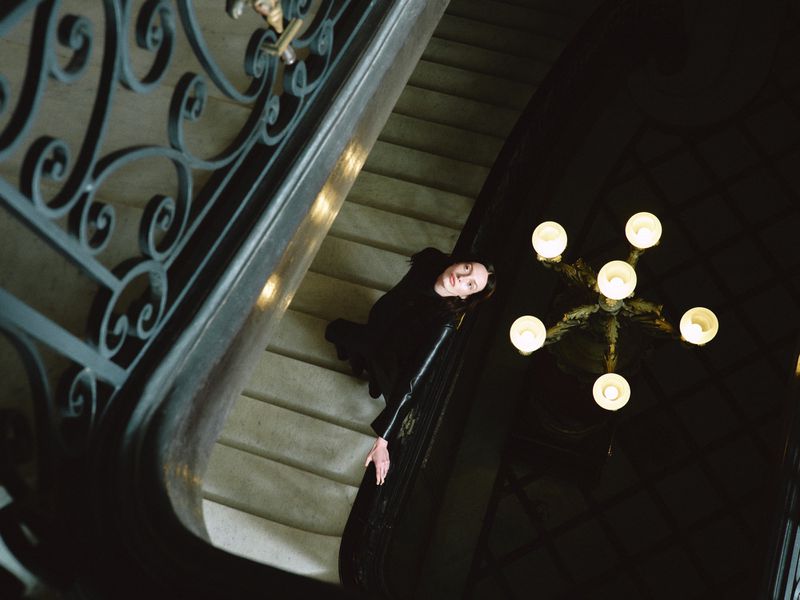 High-angle shot of a woman on a grand staircase next to an ornate chandelier for Nour Hammour Summer 26.