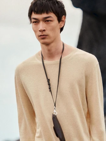 Close-up portrait of a male model wearing a beige crewneck sweater and a lanyard with a small dark pouch for Massimo Dutti.