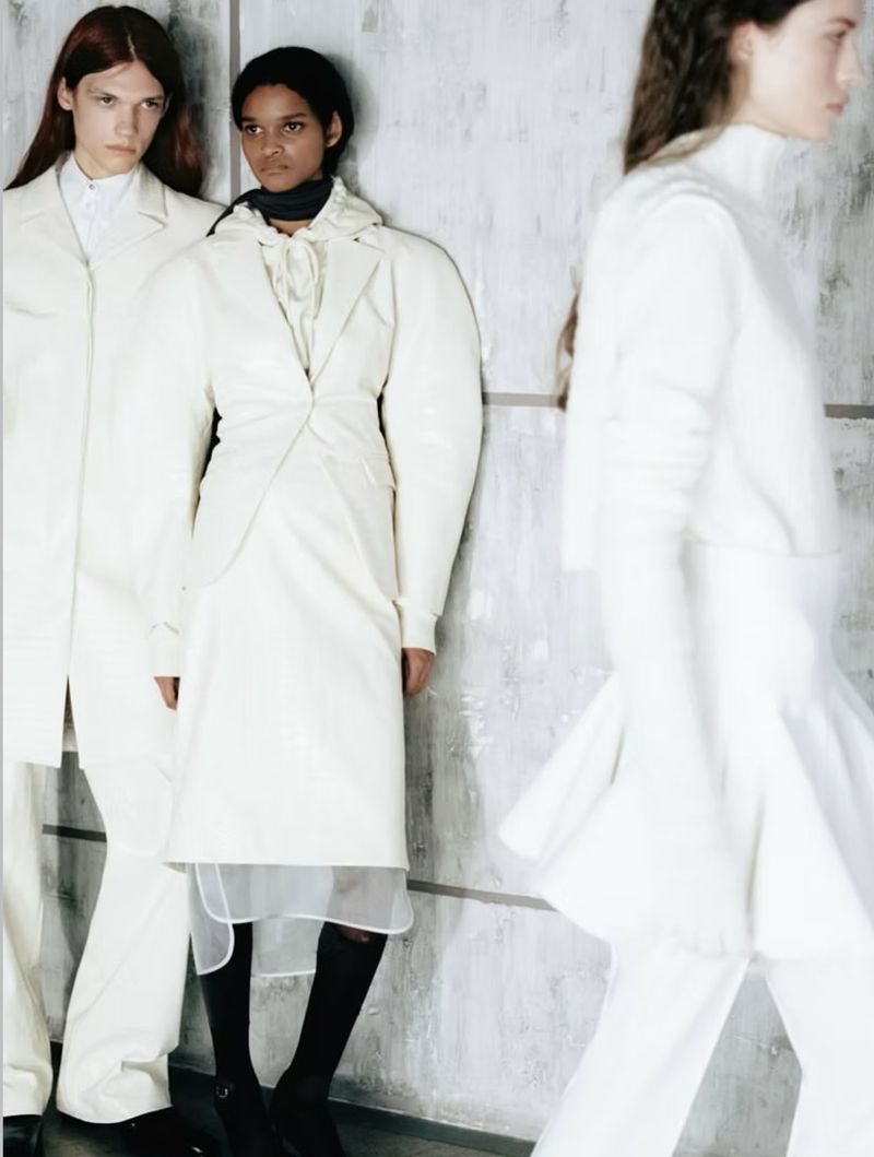 Three models wearing white designer outfits posing against a textured grey wall for Des Phemmes