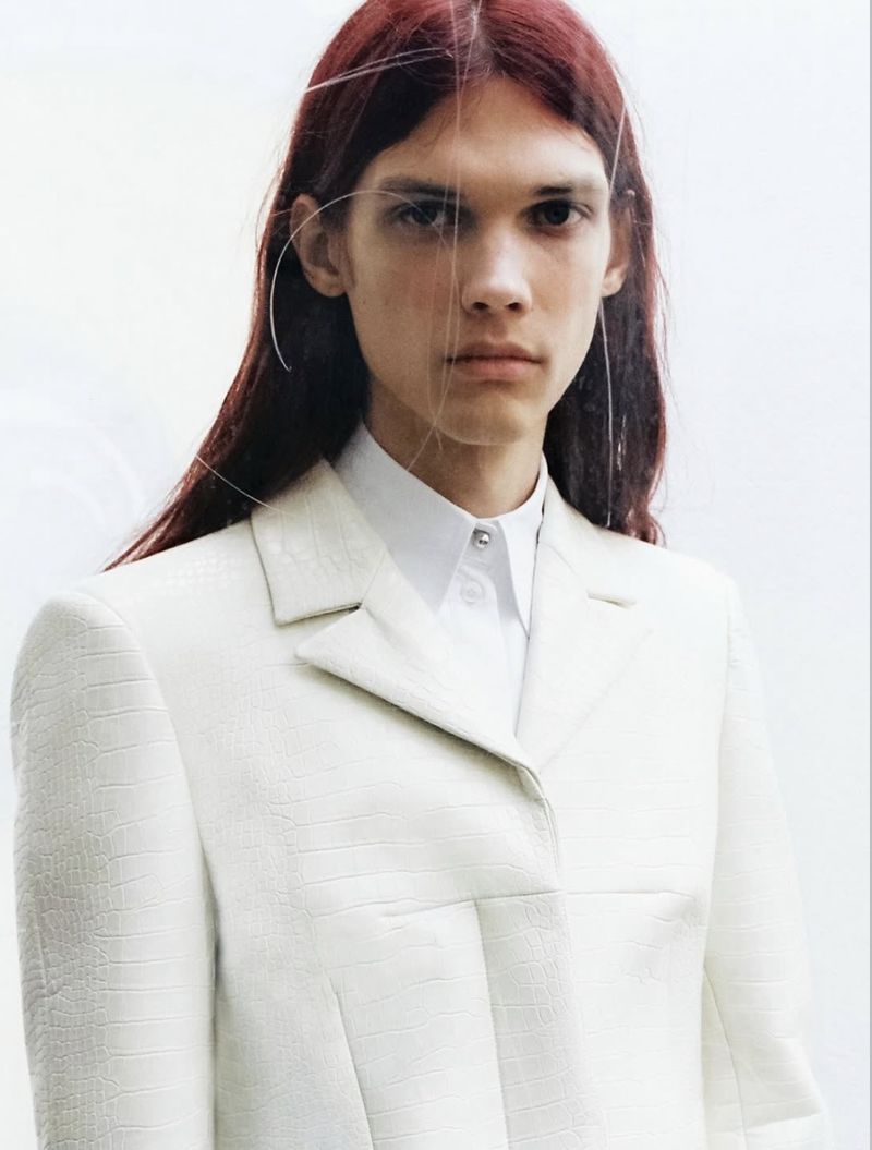 Model with long reddish-brown hair wearing a white textured jacket and button-down shirt against a plain background