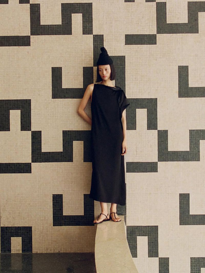 Model wearing black sleeveless dress and beanie posing against patterned tile wall for Massimo Dutti campaign